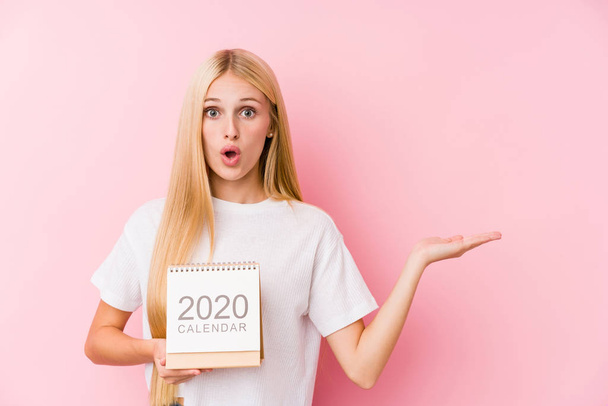 Młoda dziewczyna trzyma kalendarz 2020 pod wrażeniem posiadania miejsca kopii na dłoni. - Zdjęcie, obraz
