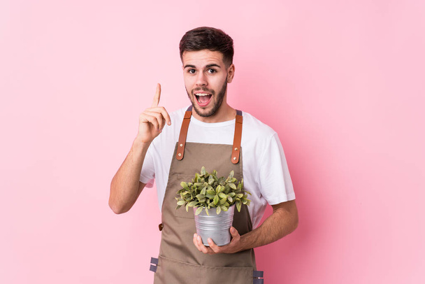 Young caucasian gardener man holding a plant isolated having an idea, inspiration concept. - Photo, Image