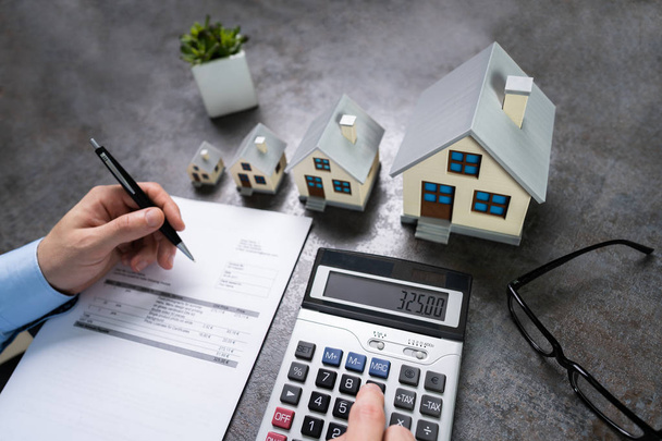Businessman Calculating Tax By Small And Big House Models - Fotó, kép