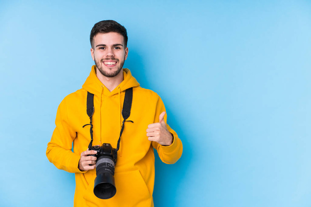 Jonge Kaukasische fotograaf man geïsoleerd glimlachen en heffen duim omhoog - Foto, afbeelding