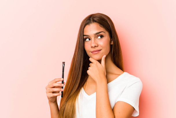 Young caucasian woman holding an skinbrush looking sideways with doubtful and skeptical expression. - Photo, Image