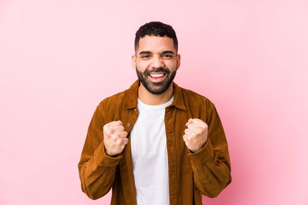 Young latin man against a pink background isolated cheering carefree and excited. Victory concept. - Fotoğraf, Görsel
