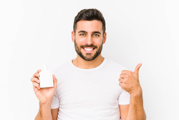 Young caucasian man holding a vitamins bottle isolated smiling and raising thumb up - Fotoğraf, Görsel
