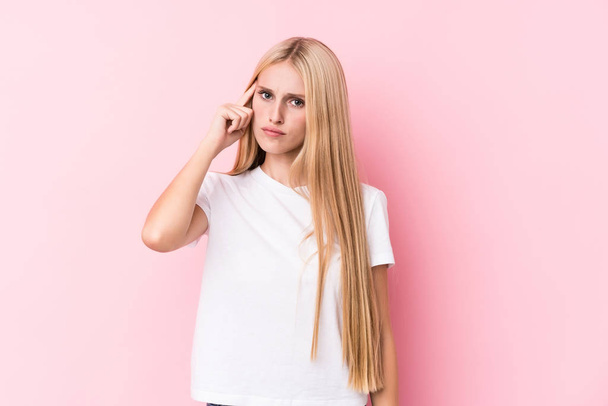 Young blonde woman on pink background pointing temple with finger, thinking, focused on a task. - Photo, Image