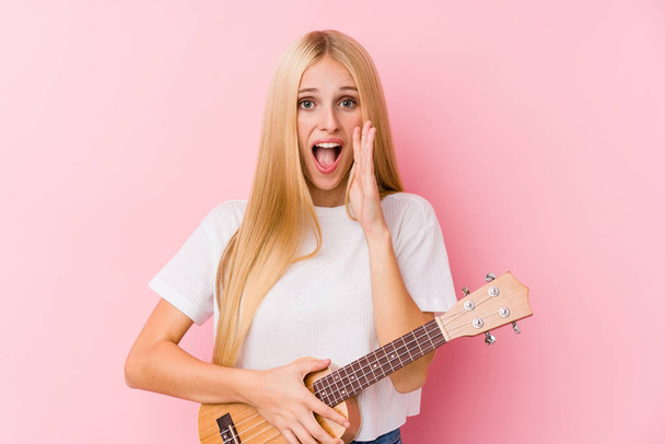 Young blonde girl playing ukelele shouting excited to front. - Photo, Image