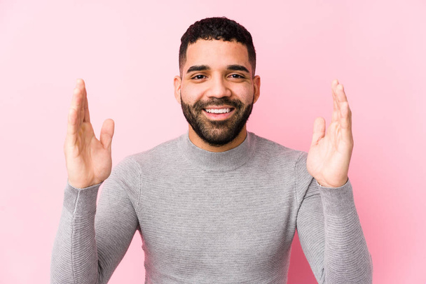 Jonge latijn man tegen een roze achtergrond geïsoleerd ontvangen van een aangename verrassing, opgewonden en het verhogen van de handen. - Foto, afbeelding