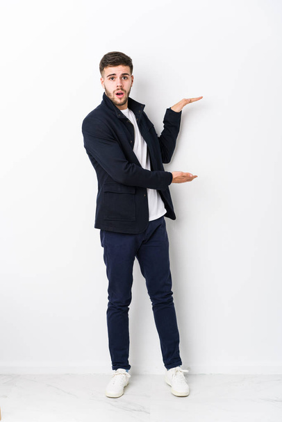 Full body young caucasian man isolated shocked and amazed holding a copy space between hands. - Photo, Image