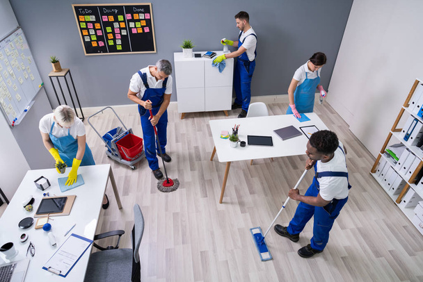 Group Of Janitors In Uniform Cleaning The Office With Cleaning Equipment - Foto, Imagen