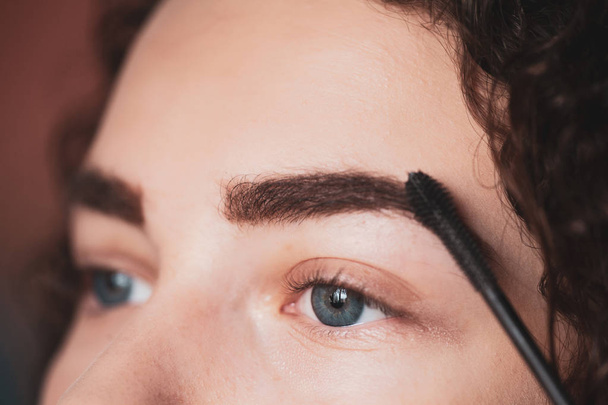 The work of a professional makeup artist. Young woman undergoing eyebrow correction procedure. Eyebrow Mascara - Foto, Imagen