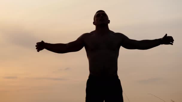 Silueta sportovce s holým trupem ukazuje jeho svaly a biceps proti obloze při západu slunce. Sport, zdraví a fitness - Záběry, video