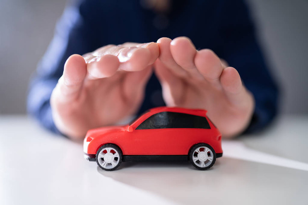 Yansıtıcı masada kırmızı oyuncak araba koruyan işadamı el - Fotoğraf, Görsel