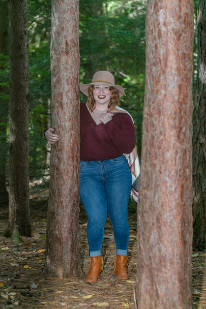 A smiling woman with a hat in a forest near the tree surrounded by branches with a blurry background - Fotografie, Obrázek