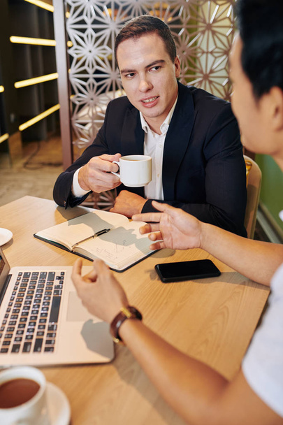 Fiatal vállalkozó iszik egy csésze kávét, és nézd meg a munkatárs elmagyarázza az üzleti ötlet - Fotó, kép