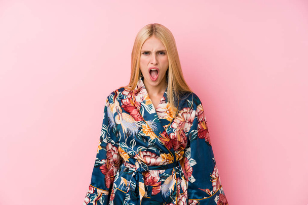Young blonde woman wearing a kimono pajama screaming very angry and aggressive. - Fotoğraf, Görsel