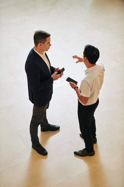 Mitarbeiter mit Smartphones in der Hand stehen in der Halle des Bürogebäudes und diskutieren Ideen für neue mobile Anwendungen - Foto, Bild
