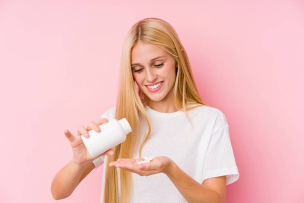 junge blonde Frau nimmt einige Tabletten isoliert auf einem schwarzen Untergrund - Foto, Bild