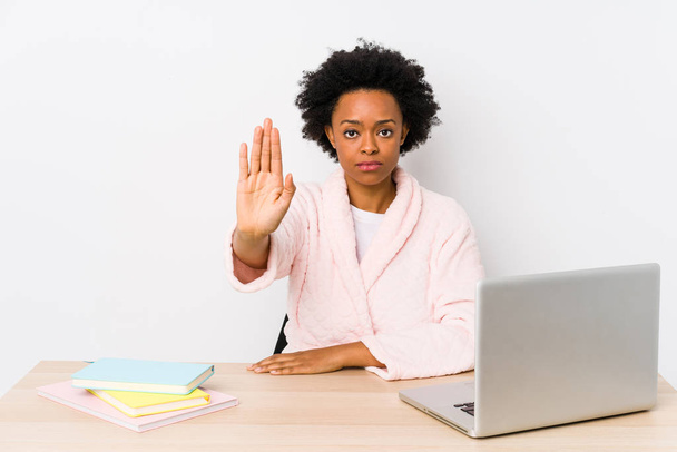 Femme afro-américaine d'âge moyen travaillant à la maison isolée debout avec la main tendue montrant le signe stop, vous empêchant
. - Photo, image