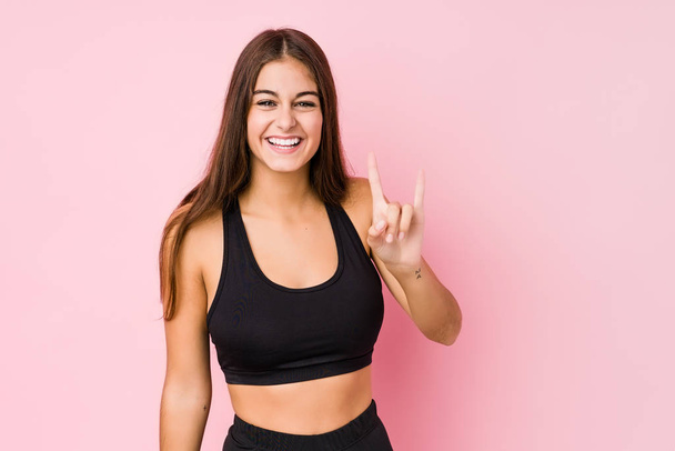 młody kaukaski fitness kobieta robi sport odizolowany pokazując a rogi gest jak a rewolucja koncepcja. - Zdjęcie, obraz