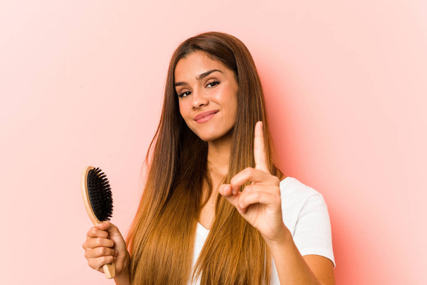 Young caucasian woman holding an hairbrush showing number one with finger. - Photo, Image