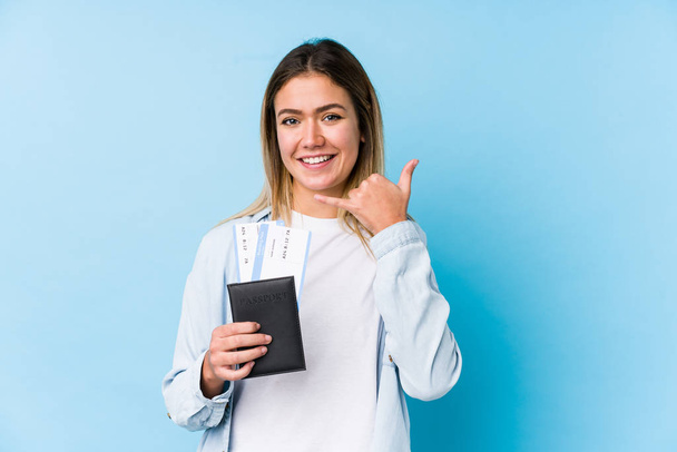 Νεαρή Καυκάσια γυναίκα που κρατά απομονωμένο διαβατήριο και δείχνει χειρονομία κινητής τηλεφωνίας με δάχτυλα. - Φωτογραφία, εικόνα