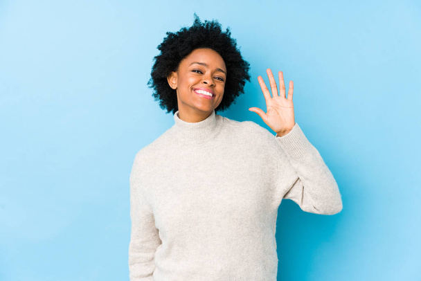 中年アフリカ系アメリカ人女性に対して青の背景隔離された笑顔陽気に示す番号5とともに指. - 写真・画像