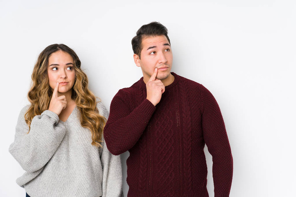 Young couple posing in a white background looking sideways with doubtful and skeptical expression. - Photo, Image