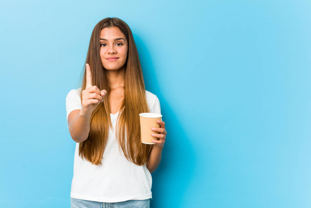 Young pretty caucasian woman holding a takeaway coffee showing number one with finger. - Fotoğraf, Görsel