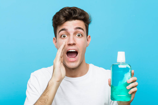 Young caucasian man holding a mouthwash shouting excited to front. - Foto, immagini