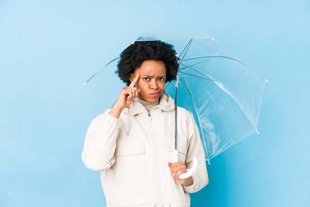 Fiatal afro-amerikai nő kezében egy esernyő elszigetelt mutató templom ujjal, gondolkodás, összpontosított feladat. - Fotó, kép