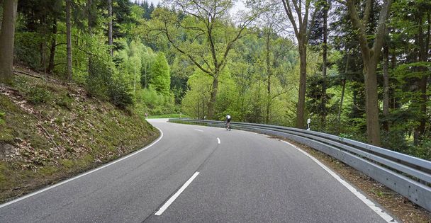 Highway through forest with turns and cyclist rides along it. Schwarzwald forest road and cyclist. Germany  - Zdjęcie, obraz