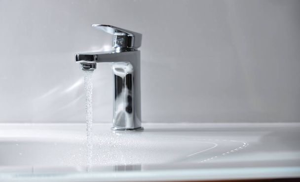 Chrome tap with open water that flows into a white modern sink - Zdjęcie, obraz