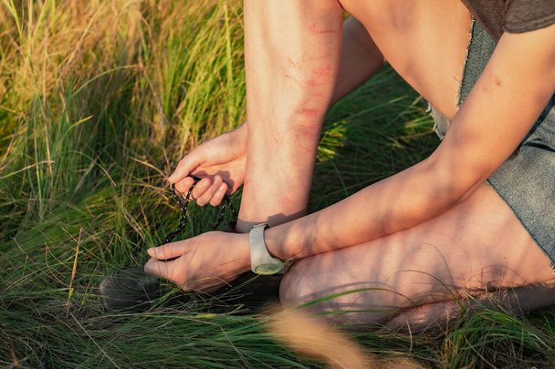 Woman ties shoelaces of hiking shoes. Close up image of female hands and legs in scratches and bruises in natural green grass background tying the laces of trekking footwear - 写真・画像