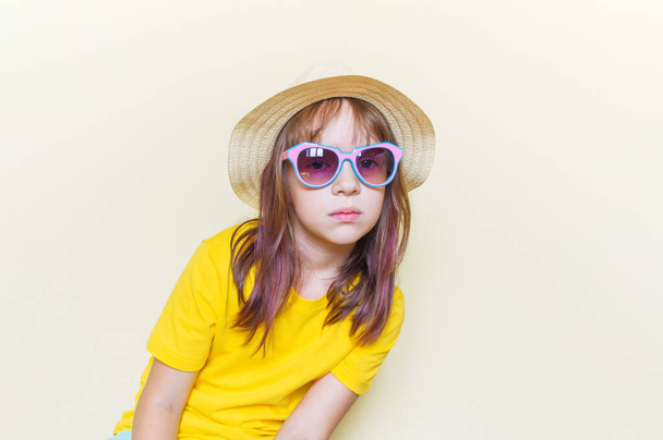 The child sits in the room on the floor emotion on his face. Little girl in a yellow T-shirt, glasses and a straw hat. - Foto, Bild