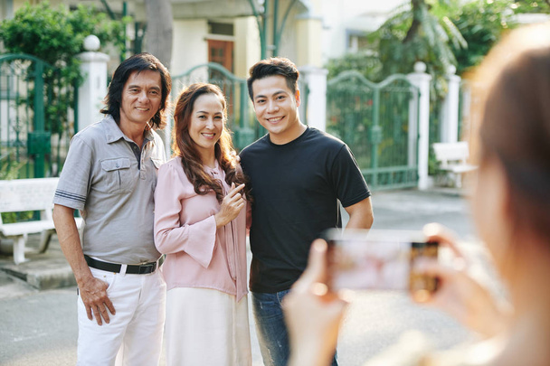 Χαμογελώντας βιετναμέζικο μεσήλικο ζευγάρι και ο ενήλικος γιος τους ποζάρουν για οικογενειακή φωτογραφία στο ύπαιθρο - Φωτογραφία, εικόνα