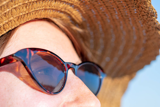 Jonge vrouw met zomerhoed en zonnebril, close-up portret. Zomervakantie, zonnig weer, vakantie sfeer concept - jong meisje hoofd met sproeten in retro bril - Foto, afbeelding