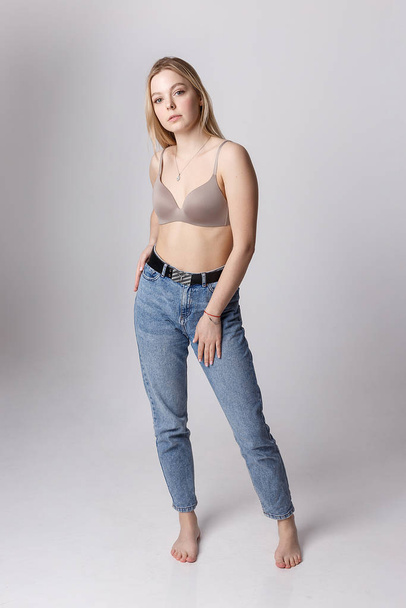 sexy caucasian woman posing in beige lingerie, blue jeans on white background - 写真・画像