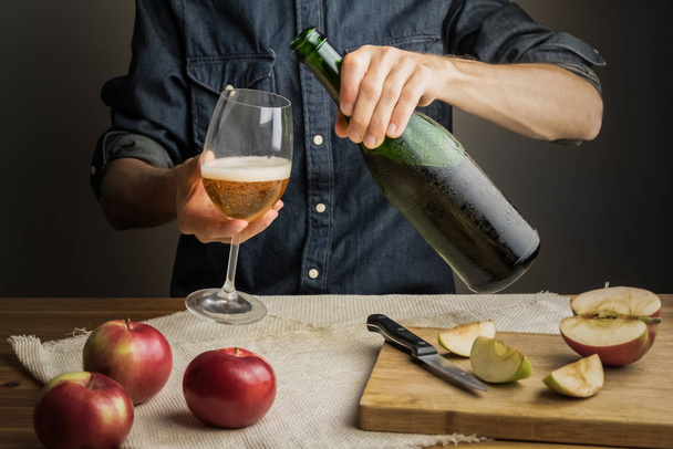 Male hands pouring premium cidre in wine glass above rustic wood table. Tasting vintage apple cider out of ice cold bottle - Valokuva, kuva