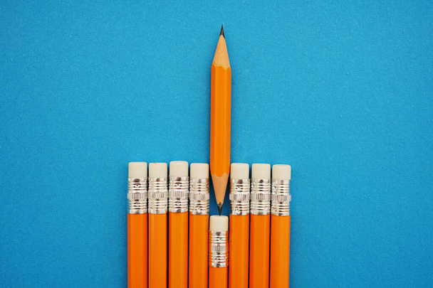 inverted one sharp small Pencil  rises above the rest yellow pencils. isolated on blue paper background - Fotoğraf, Görsel