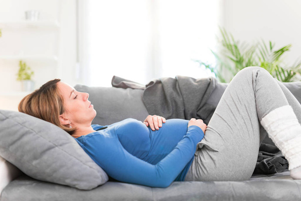 Pregnant tired exhausted woman with stomach issues at home on a  - 写真・画像
