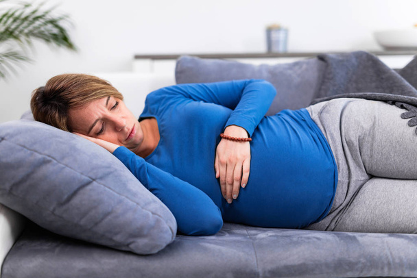 Pregnant tired exhausted woman with stomach issues at home on a  - Photo, Image