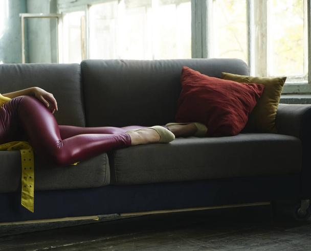 detail of woman wearing red leather  pants and  white low shoe. female lie on gray coach, sofa with two pilliows. open window. sunny day. no face. - Photo, image