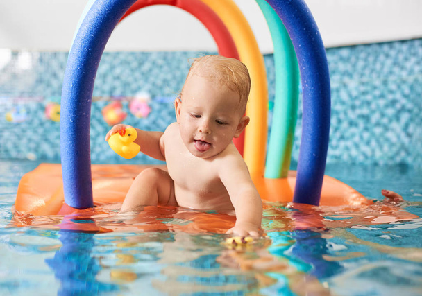Portré egy aranyos kisfiú kezében a gumi játék egy úszó színes konstrukció a medencében próbál keményen nyúlni a többi játék a vízben. A biztonságos úszás koncepciója - Fotó, kép
