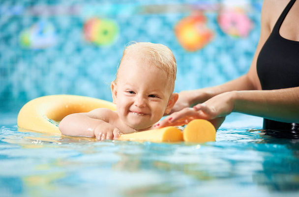 Portret początkującego pływaka w basenie. Słodki chłopczyk unosi się w wodzie z pomocą makaronu basenowego i jego mamy. Rozwijanie miłości do sportu. - Zdjęcie, obraz