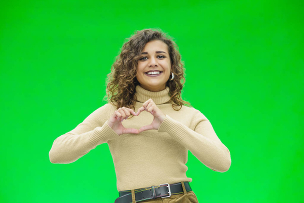 Gorgeous young woman over a green background doing a heart shape with her hands. - Φωτογραφία, εικόνα