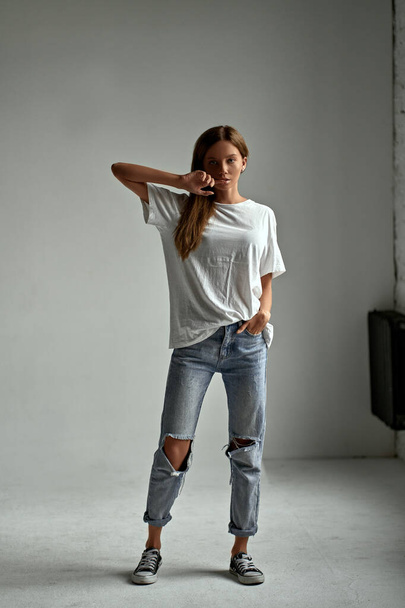 Portret van elegant aantrekkelijk meisje in shirt, sneakers en jeans. Sexy mode stijl vrouw model poseren op witte achtergrond in studio - Foto, afbeelding