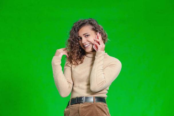 Friendly female talking on her cell phone, standing against green background. - Foto, imagen