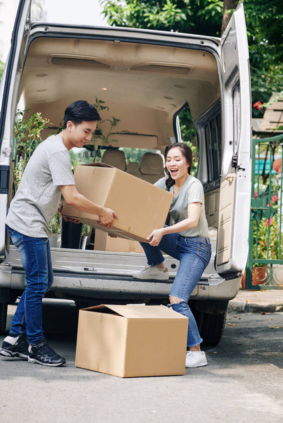 Cheerful young Asian couple unloading truck with their belongings when moving in new house - Photo, Image