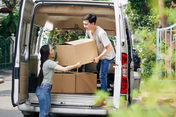 Joven mujer asiática ayudando novio a tomar caja de cartón fuera de coche
 - Foto, Imagen