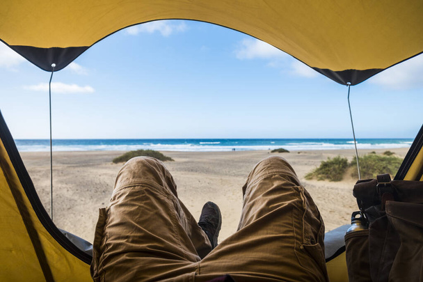 Ponto de vista com o homem deitado dentro de uma tenda desfrutando de relaxar e aventura no acampamento livre com praia e mar
 - Foto, Imagem