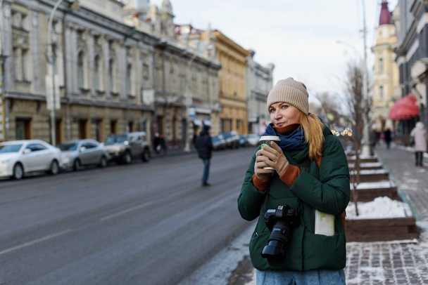街の歴史的中心部にあるカメラと地図のある冬服の少女が路上でコーヒーを飲んでいます - 写真・画像